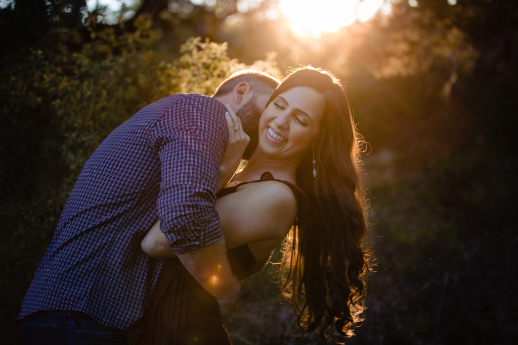 Couple embraces at Westcave Discovery Center for engagement photos with sun behind them.  Photography by Shannon Cain Photography