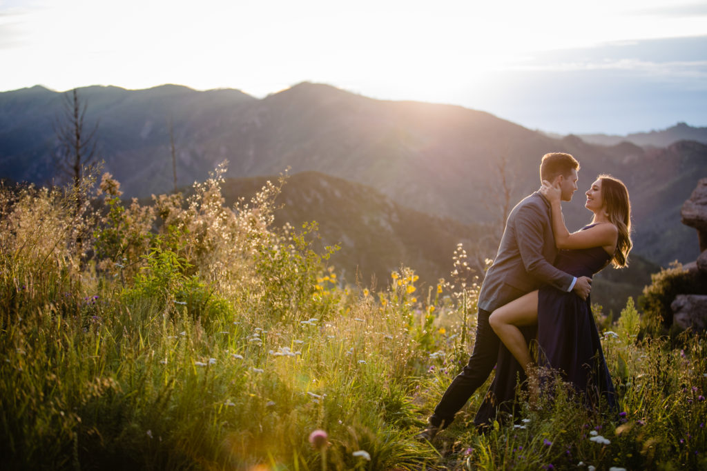 Couple embracing for engagement photos at Monjeau Lookout in Ruidoso, New Mexico with wildflowers surrounding them.  Photo by Shannon Cain Photography