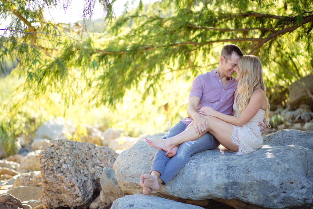 Couple cuddled up in dressy/casual outfits under a cypress tree at Pedernales Falls State Park.  Photography by Shannon Cain Photography
