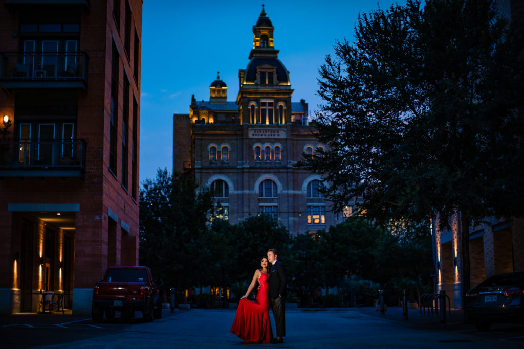 Couple taking engagement photos in red dress and tux at The Pearl Historic District in San Antonio, TX.  Photo by Shannon Cain Photography