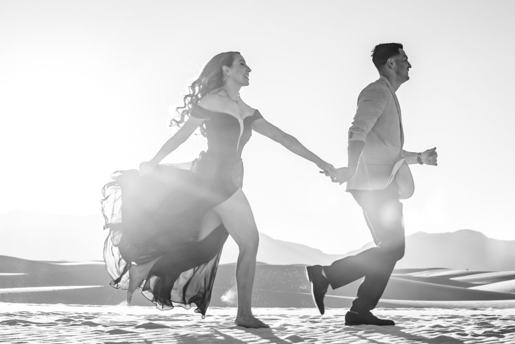 Bride and Groom running at The White Sands National Park at sunset for Adventure Engagement Session.  Photography by Shannon Cain Photography.  Hair and Makeup by Glam on Demand.