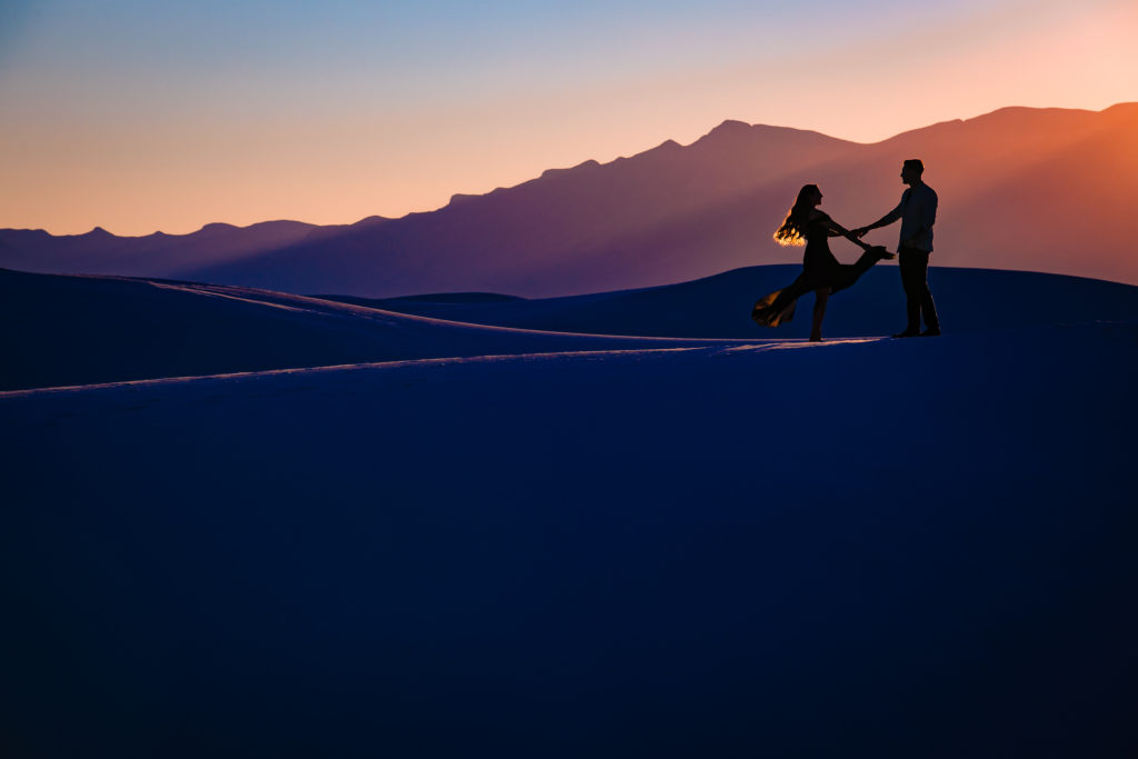 Bride and Groom twirling at The White Sands National Park at sunset for Adventure Engagement Session.  Photography by Shannon Cain Photography.  Hair and Makeup by Glam on Demand.