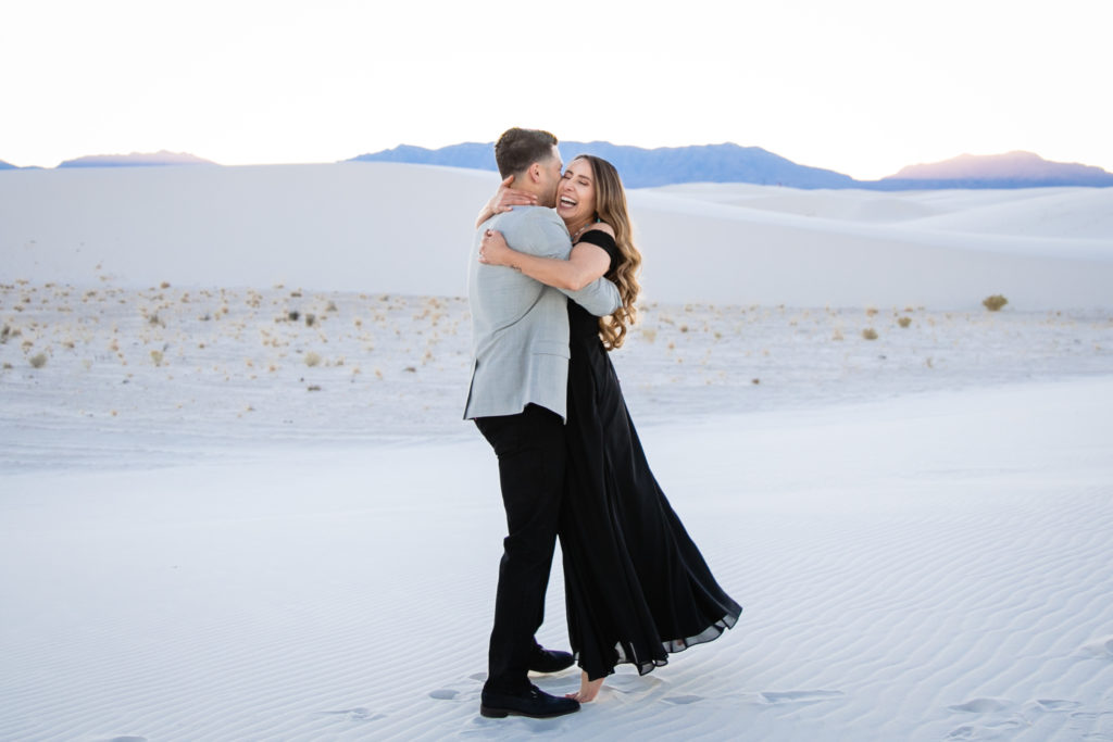 Bride and Groom embracing at The White Sands National Park at sunset for Adventure Engagement Session.  Photography by Shannon Cain Photography.  Hair and Makeup by Glam on Demand.