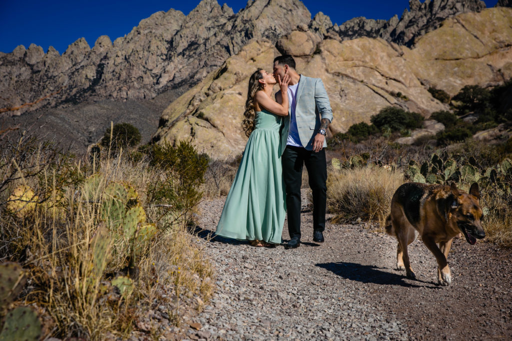 Bride and Groom walk dog at The Organ Mountains in Las Cruces, NM at sunset for Adventure Engagement Session.  Photography by Shannon Cain Photography.  Hair and Makeup by Glam on Demand.